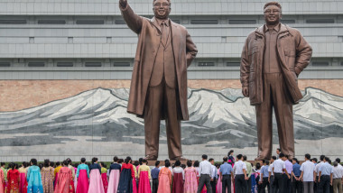 oameni in fata a doua statui uriase cu fostii conducători din coreea de nord