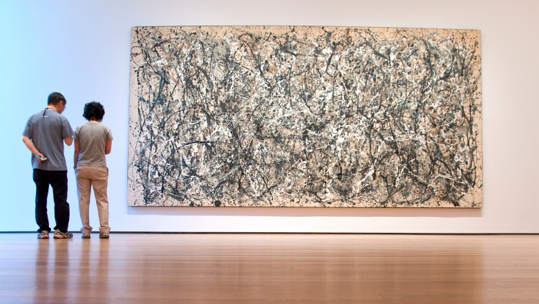 Două persoane stau lângă un tablou de Jackson Pollock la Muzeul de Artă Modernă din New York.