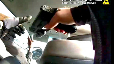 Mâna unui polițist care îndreaptă un pistol spre șoferul unei mașini în mișcare