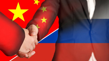 Doi bărbați dau mâna având pe fundal steagul Chinei și al Rusiei.