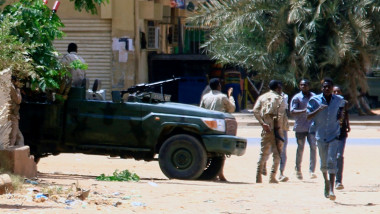 Oameni merg pe lângă vehicule militare în capitala Sudanului pe 15 aprilie 2023.