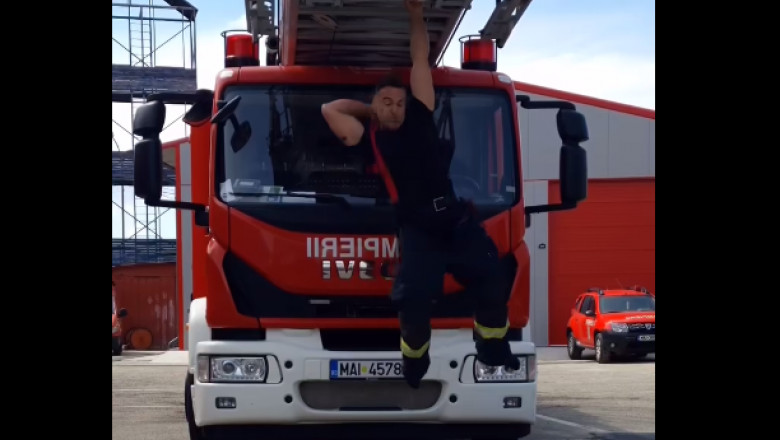 un pompier se imbraca in timp ce sta agatat de scara masinii de interventie