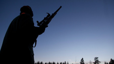 Un vânător cu o pușcă pe un câmp pe timp de noapte.