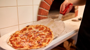 un bucatar scoate pizza din cuptor si o pune pe farfurie