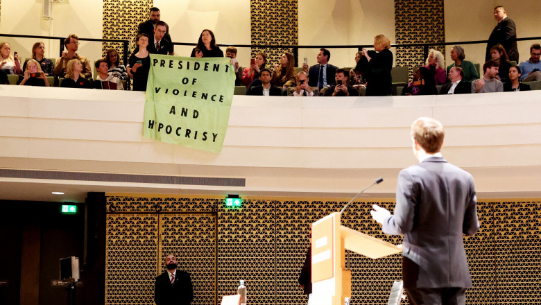 Emmanuel Macron privește spre protestatari dintr-o tribună care afișează un banner