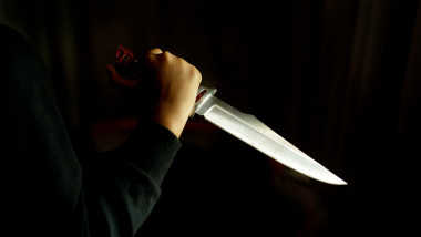 Close-up of a hand holding a large knife in a dark room. Concept of crime and violence.