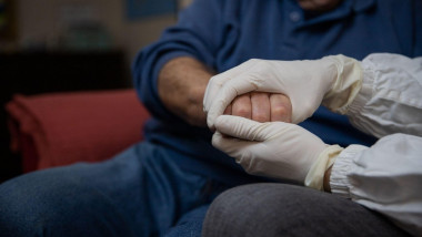 Un medic ține mâna unui pacient vârstnic.