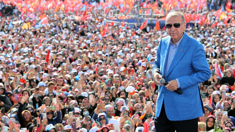 erdogan in sacou si ochelari de spare pe scena lșa miting politic cu multi oameni in spate