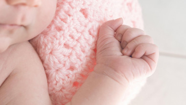 Detail of the hand of a baby girl wrapped in a pink wool blanket