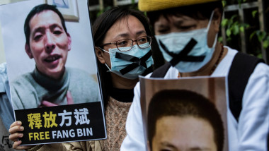 oameni cu măști marcate cu X țin în mână un banner pentru eliberarea lui Fang Bin