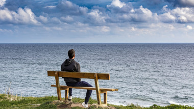 un bărbat stă pe o bancă și se uită spre mare