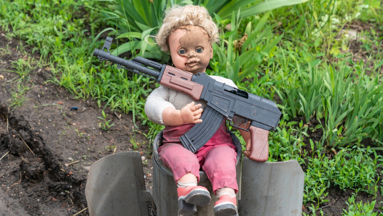 Păpușă cu o armă de jucărie așezată pe ea