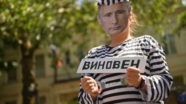 Protestatar îmbrăcat într-o uniformă de prizonier cu fața lui Vladimir Putin, ținând un banner cu un cuvânt în limba rusă