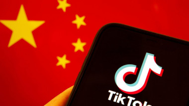 Emblema TikTok văzută pe ecranul unui telefon mobil cu fundalul steagului chinezesc pe fundal.