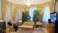 Vladimir Putin stă pe un fotoliu și se uită la televizor într-o cameră cu draperii aurii