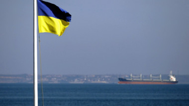 O navă traversează coridorul agreat pentru exporturile ucrainene pe Marea Neagră, lângă Portul Odesa, văzută de lângă un drapel ucrainean pe 20 februarie 2023.