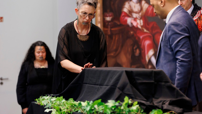 Femeie cu tatuaj facial atinge o cutie acoperită de un văl negru