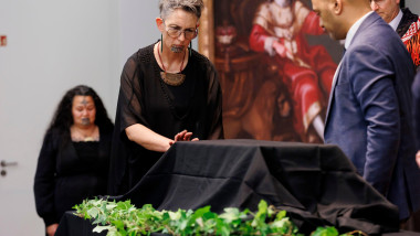 Femeie cu tatuaj facial atinge o cutie acoperită de un văl negru