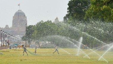Persoane aleargă prin jeturile de apă care udă un gazon în New Delhi, India, pe 12 iunie 2023.