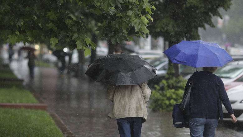 Două femei se apără de ploaie cu umbrelele în timp ce merg pe un trotuar din București pe 17 iunie 2020.