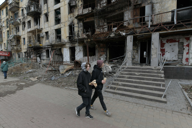 Copii merg prin fața unei clădiri distruse
