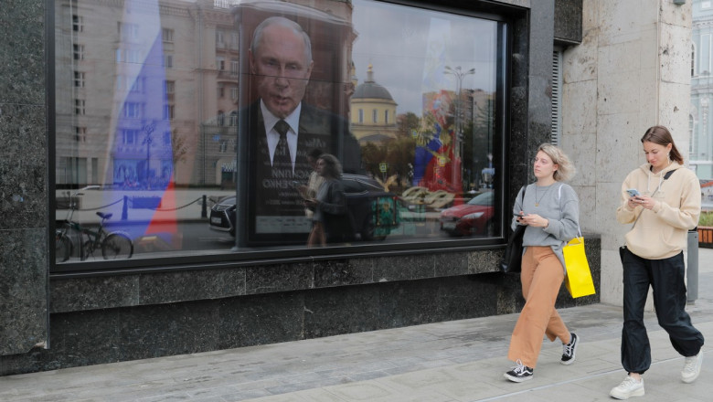doua femei trec pe langa un ecran tv in rusia