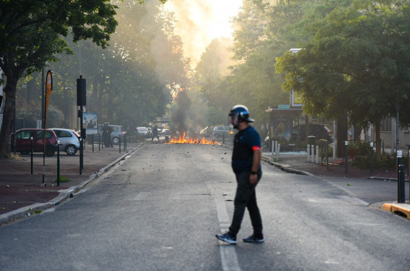 un polițist din profil pe o stradă în depărare arde un foc