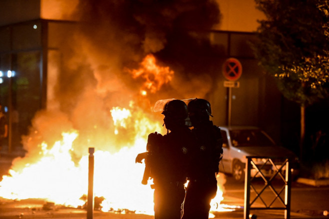 doi jandarmi echipați privesc spre un incendiu pe o stradă din Paris pe timp de noapte