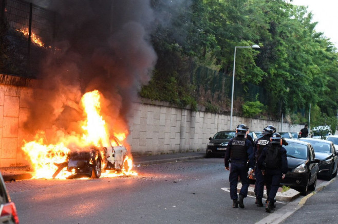 jandarmi francezi trec pe lângă o mașină în flăcări