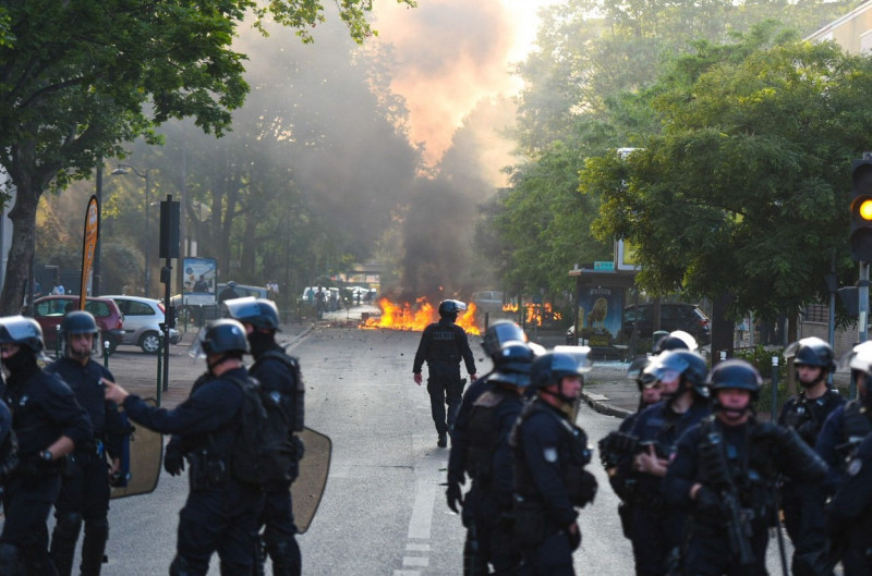 Jandarmi francezi pe o stradă privesc spre o mașină incidendiată în depărtare