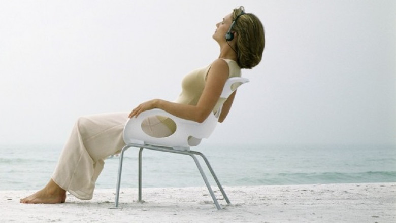 femeie sta pe un scaun pe plaja si asculta la casti