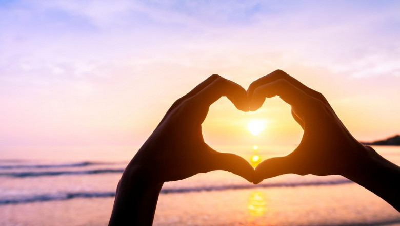 Shape of heart done with silhouette of hands on a beach with sunset sun and colors - Symbol of love - Romantic travel
