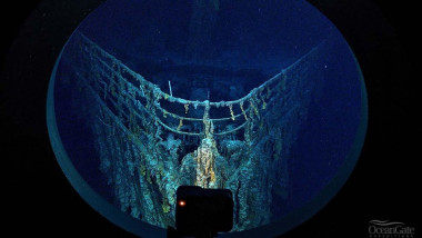 Hubloul unui submersibil și o cameră care filmează imaginea de afară cu prova Titanicului