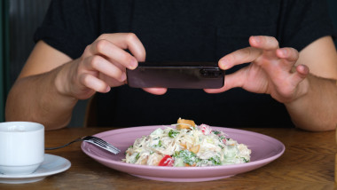 un baiat fotografiaza cu telefonul mâncarea dintr-o farfurie