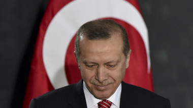 Erdogan privește în jos și zâmbește cu steagul Turciei în spate
