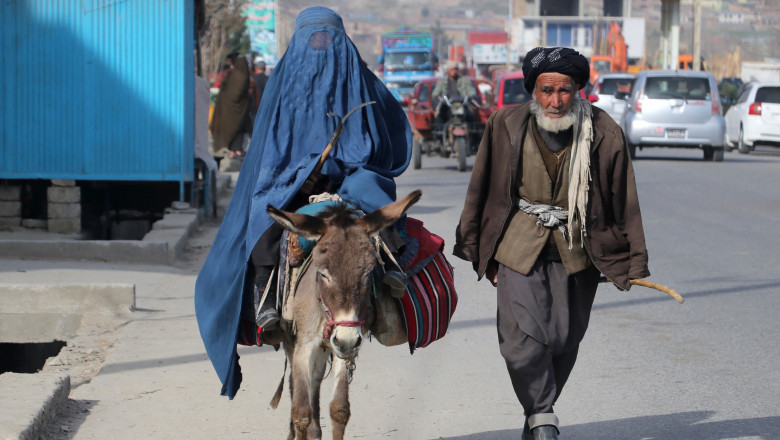 A man walks beside a burqa-clad woman riding a donkey along a street in Fayzabad