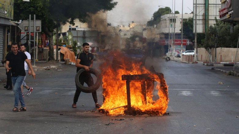 People make a fire with car tires around Israeli military vehicles during a clash broke out between Israeli forces and Palestinians in Nablus, West Bank