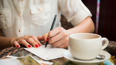 o femeie scrie o carte postala cu o cafea langa