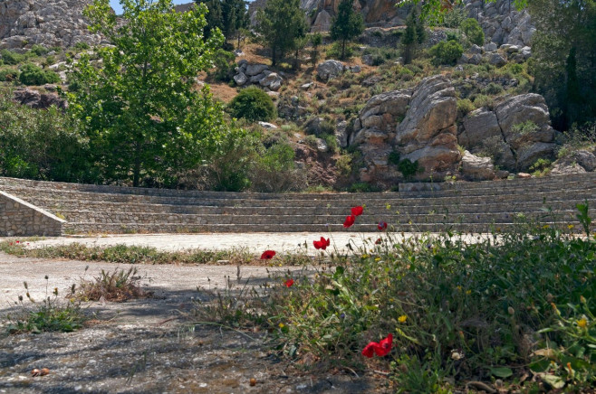 The stone amphitheatre at the Elephant Museum and caves, Tilos. Dodecanese. Greece. With poppies in foreground.. May 2022. Spring