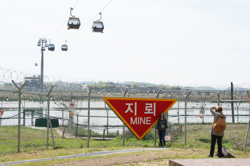 turiști își fac poze în fața unui panou care avertizează prezența minelor anti-personal în Zona Demilitarizată dintre cele două Corei