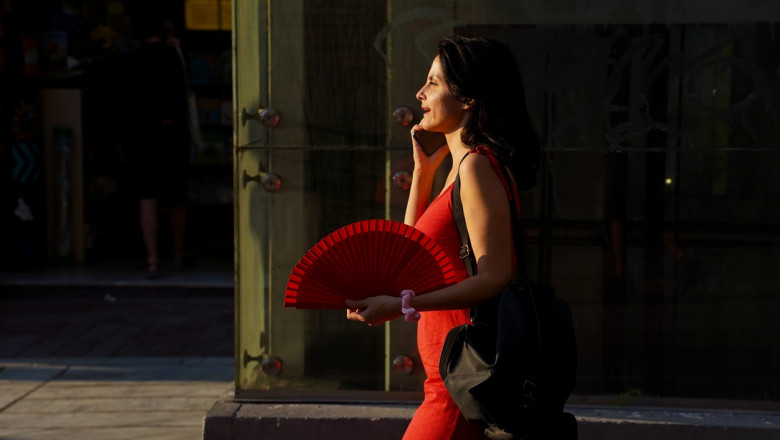 Femeie îmbrăcată în roșu cu un evantai roșu pe timp de vară în Atena