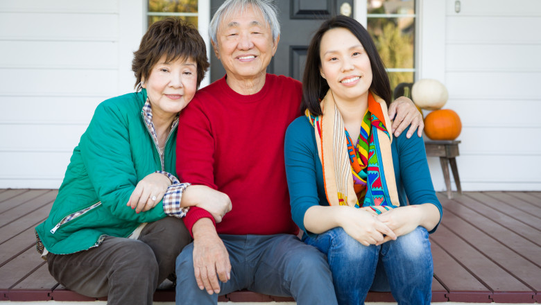 un bărbat în vârstă, o femeie în vârstă și o tânără, toți asiatici, chinezi, stau pe prispa casei