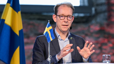 ministrul suedez de externe Tobias Billstrom stă la o masă și în imagine se văd și două stegulețe cu steagul Suediei