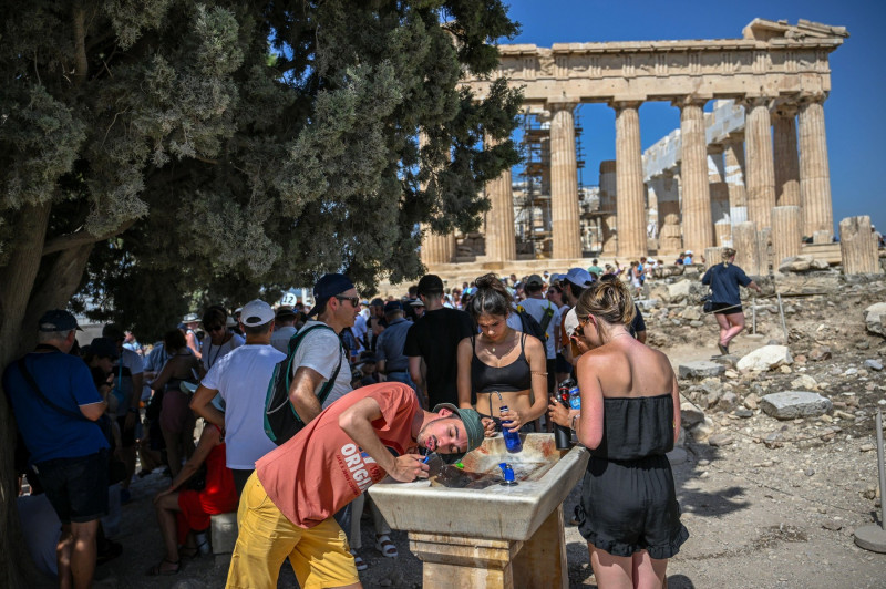 Athen, Greece. 14th July, 2023. Tourists cool off at a water fountain during their visit to the Parthenon Temple on the Acropolis Hill on this hot day. The Ministry of Culture has decided to close the archaeological site during the hottest hours of the da