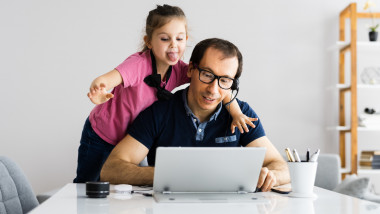 o fetita scoate limba si se distreaza langa tatal ei care lucreaza la laptop