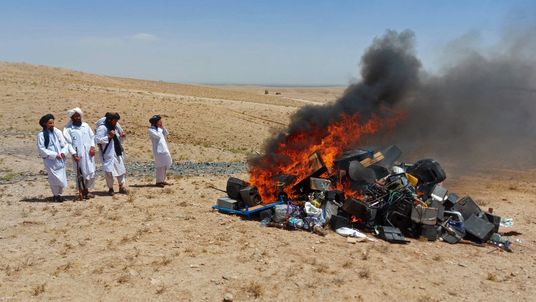 un grup de talibani se uita la un morman de instrumente si echipamente muzicale care ard