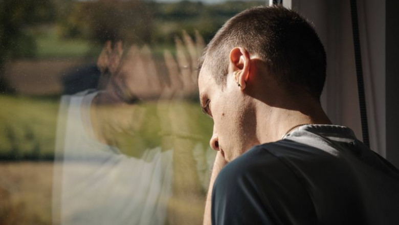 un bărbat se uită pe fereastră cu capul sprijinit de geam