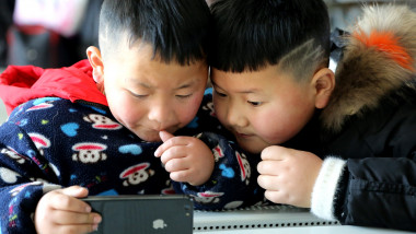 doi copii asiatici se uita la ecranul unul smartphone foarte concentrati