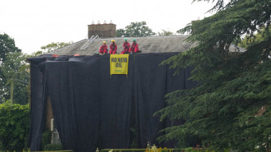Patru oameni cu un banner galben pe o casă acoperită de fâșii de țesătură neagră