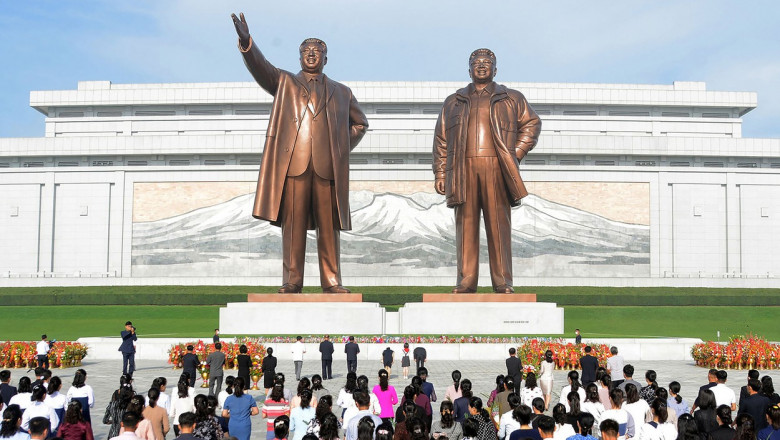 nord-coreeni în fața statuilor dictatorilor Kim